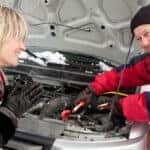 Man helping woman jumpstart her dead car battery on the side of the road