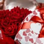 Valentine's day. Red roses in a white box in the form of a heart on the background of foil balls. A gift for women on a holiday. The concept of delivering flowers. floristry and flower shops.