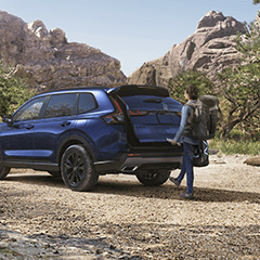 A person closing the trunk of a blue Honda CRV