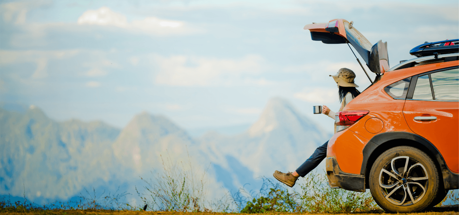 Woman sitting in the back of an orange car looking over the mountains