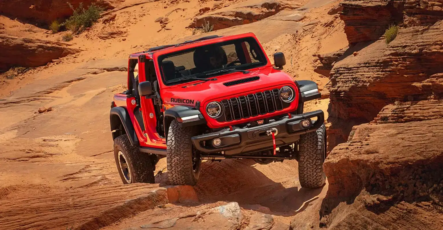 A red 2026 Jeep Wrangler traversing through rocky terrain