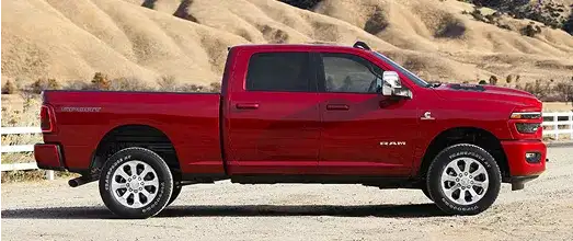 Red Ram pickup parked on a dirt road beside a wooden fence