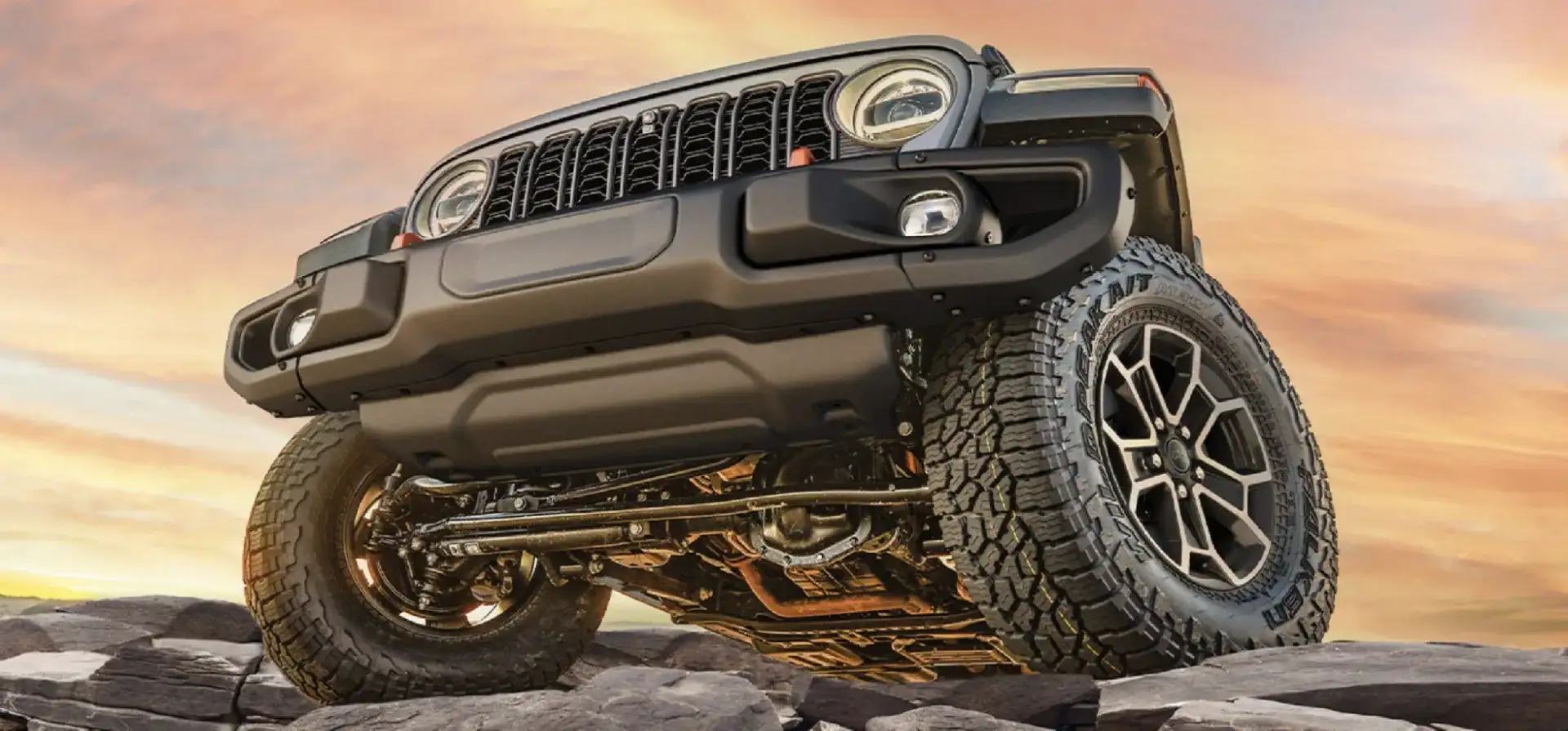 Low angle view of a Jeep Gladiator climbing over rocks, showing its skid plates, solid axles, and all-terrain tires