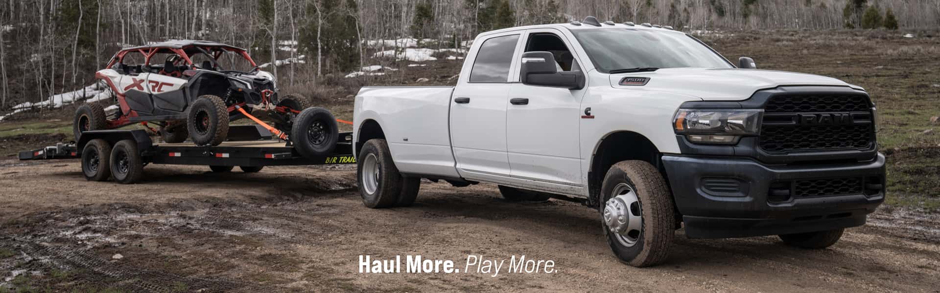 Haul More. Play More. -2025 3500 (D2) Tradesman Crew Cab Dually in Bright White parked on a dirt road, towing a flatbed trailer loaded with a UTV, with a winter forest, mountains and clouds visible behind.