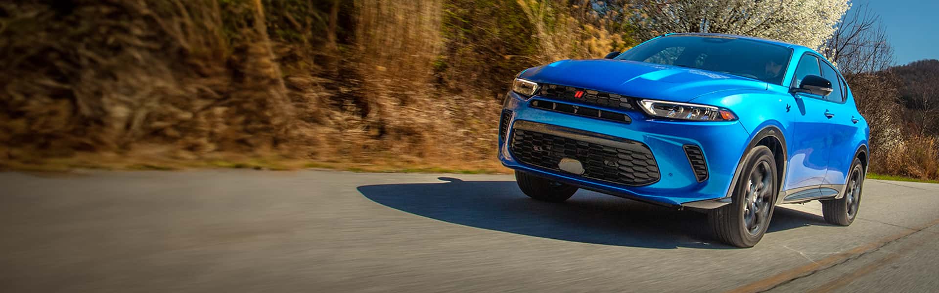 2024 Hornet R/T in Blue Bayou driving along a road with a blossoming tree, hills and clear blue sky visible in the distance