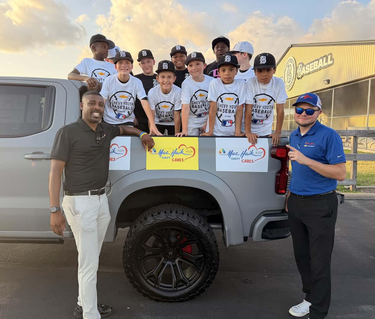 Two members of dealership on each side of a truck with kids from the Chevy Charity group in the bed of the truck