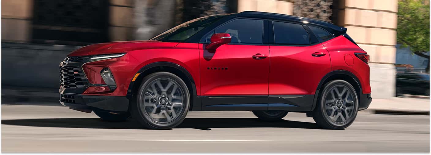 Red 2026 Chevrolet Blazer with a black roof driving on a city street, shown from a front three-quarter angle.