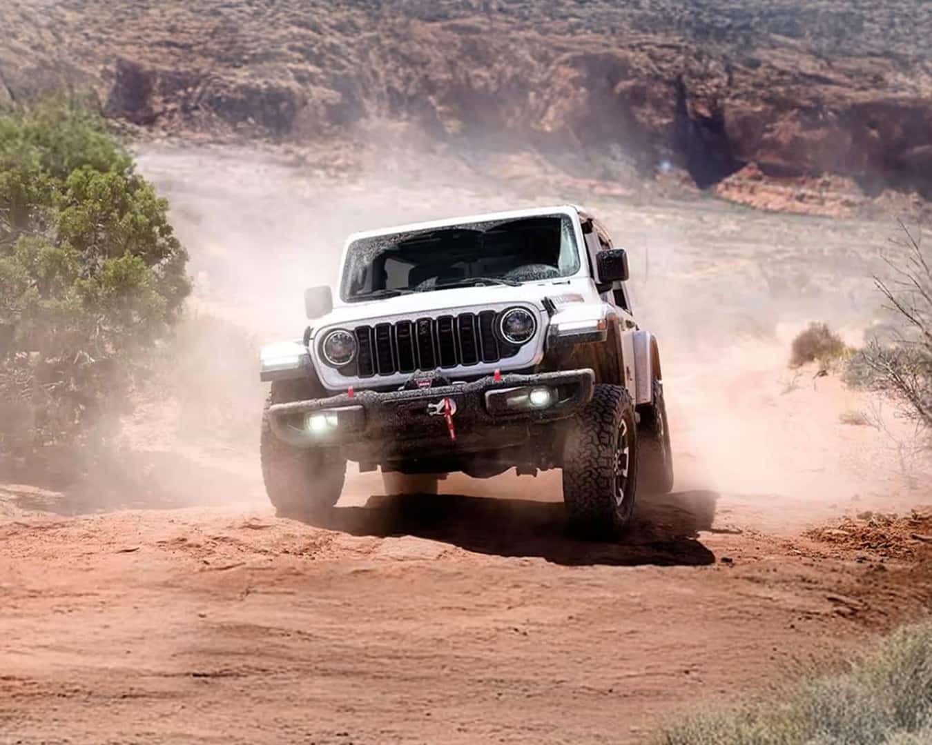 Head on shot of the 2026 Jeep Wrangler driving off-road kicking up dust.