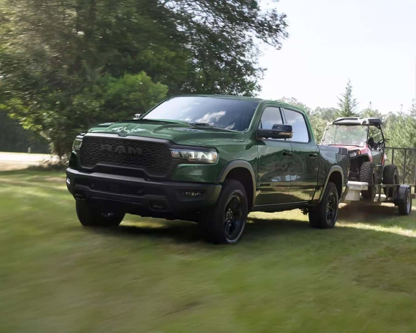 Front 3/4 shot of the 2026 RAM 1500 driving on grass towing off-road vehicle.