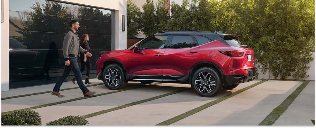Rear three-quarter view of a red 2026 Chevrolet Blazer with a black roof parked in a residential driveway.