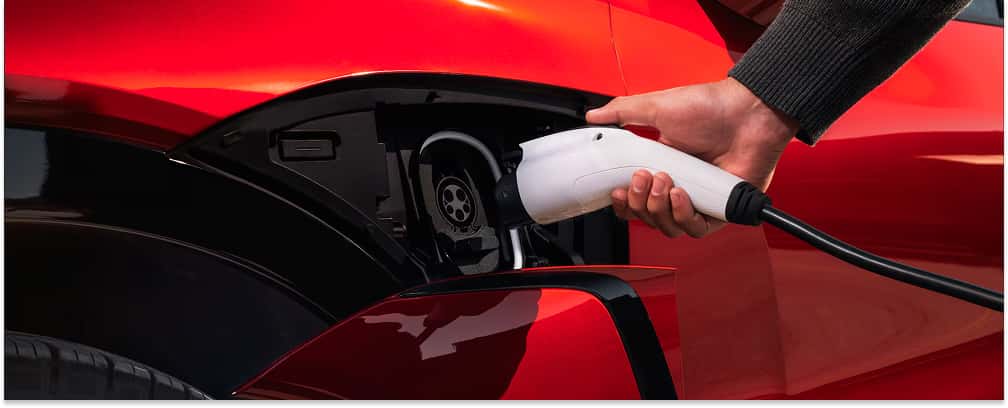 Close-up of a person charging a red 2026 Chevrolet Blazer EV at its open charging port.