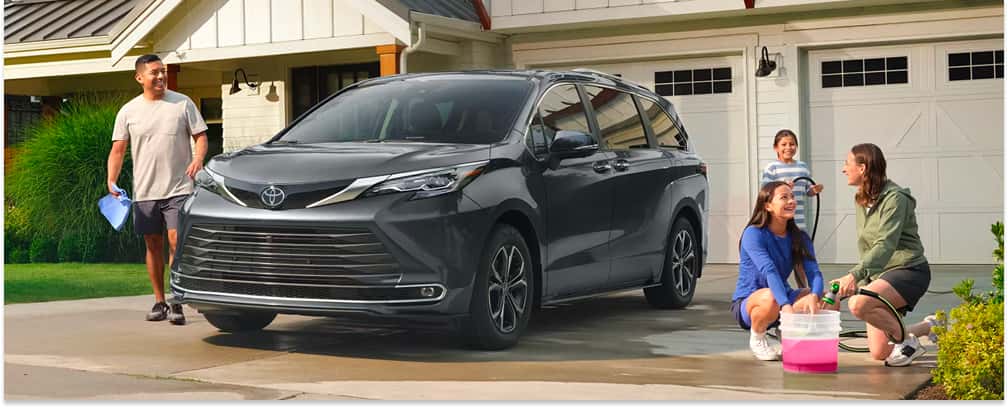 Dark gray 2026 Toyota Sienna parked on a residential driveway being washed by a family.
