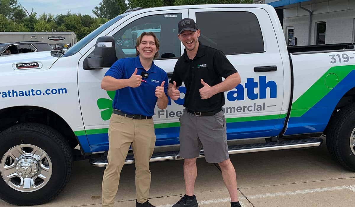 two employees giving thumbs up standing in front of fleet truck