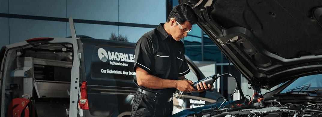 A Mercedes-Benz service technician working under the hood of a vehicle