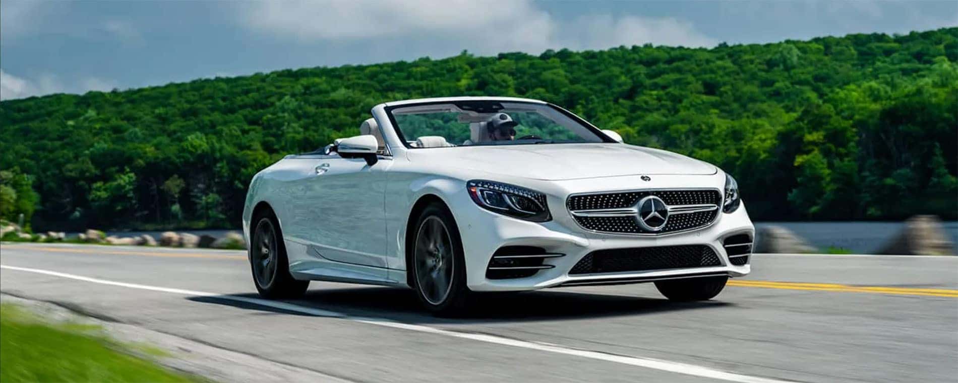 A Mercedes-Benz vehicle on the road with the top down and trees in the background