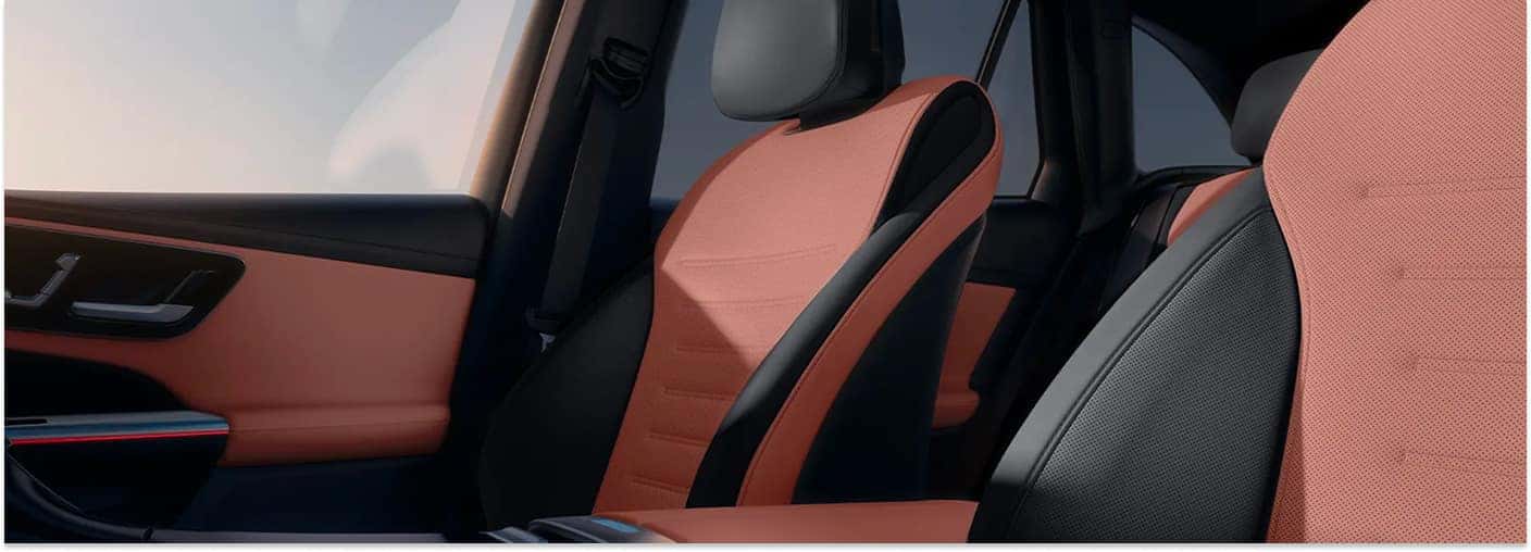 The upscale interior of a 2026 Mercedes-Benz GLC SUV features sporty two-tone black and sienna brown leather seats with perforated inserts, complemented by a matching door panel and integrated ambient lighting.