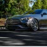 Front three-quarter view of a matte gray 2026 Mercedes-Benz C-Class sedan driving on a suburban street.