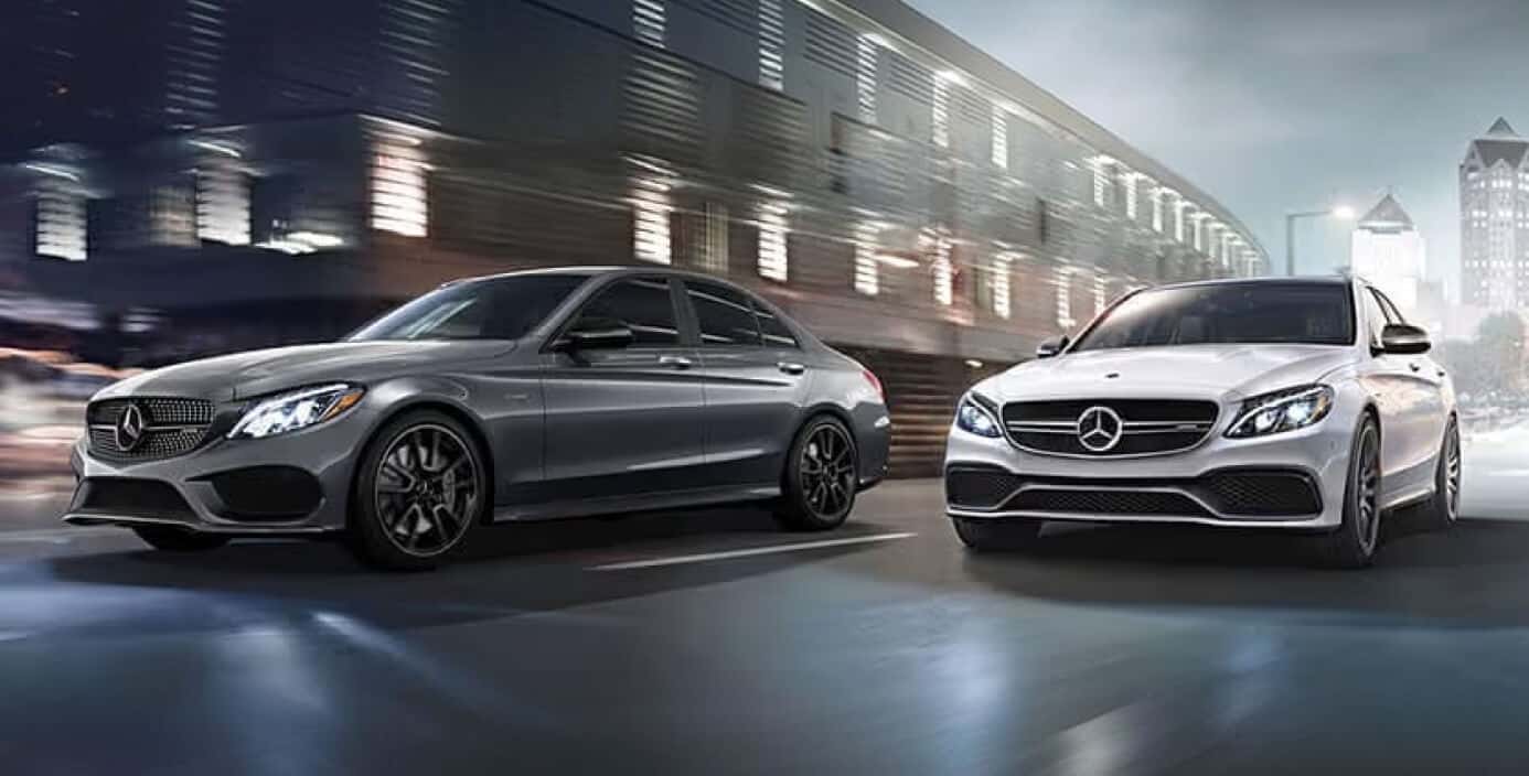 Two Mercedes AMG cars driving side-by-side down a foggy city street at night.