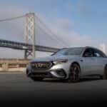 The High-Performing 2026 Mercedes AMG(R) E53 HYBRID Wagon Driving A Deserted Parking Lot, In View Of Storage Units And A Tall Bridge