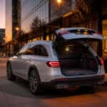 2027 Mercedes-Benz E 450 4MATIC All-Terrain wagon in silver at dusk in a modern urban business corridor