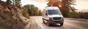 sprinter van driving on road with trees in background