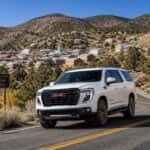 2026 GMC Yukon XL on the winding NV-342 mountain grade between Carson City and Virginia City, Nevada, with autumn sagebrush and historic mining town skyline in background