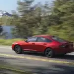 Red 2026 Honda Accord Sport L Hybrid driving on a country road by a lake