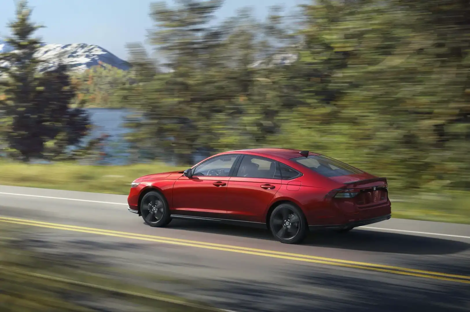 Red 2026 Honda Accord Sport L Hybrid driving on a country road by a lake