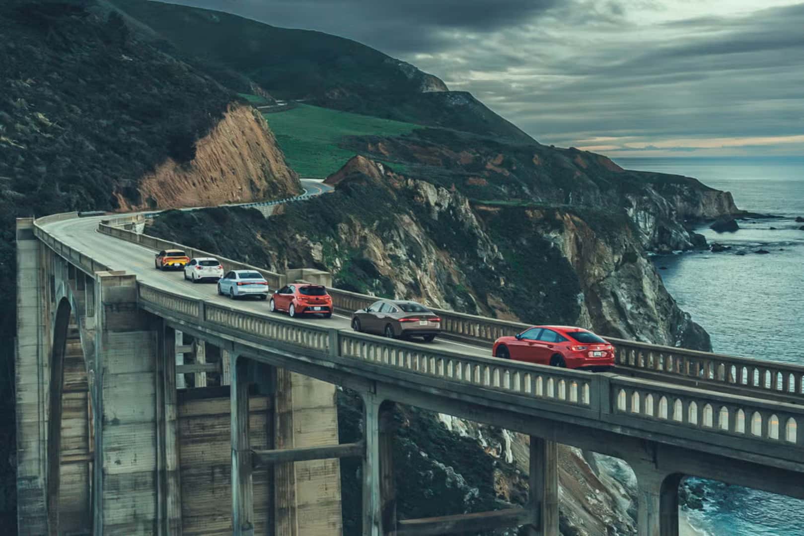 A Long Bridge With All The Compared Cars From The Car And Driver Comparison Review, Driving Under A Stormy Sky