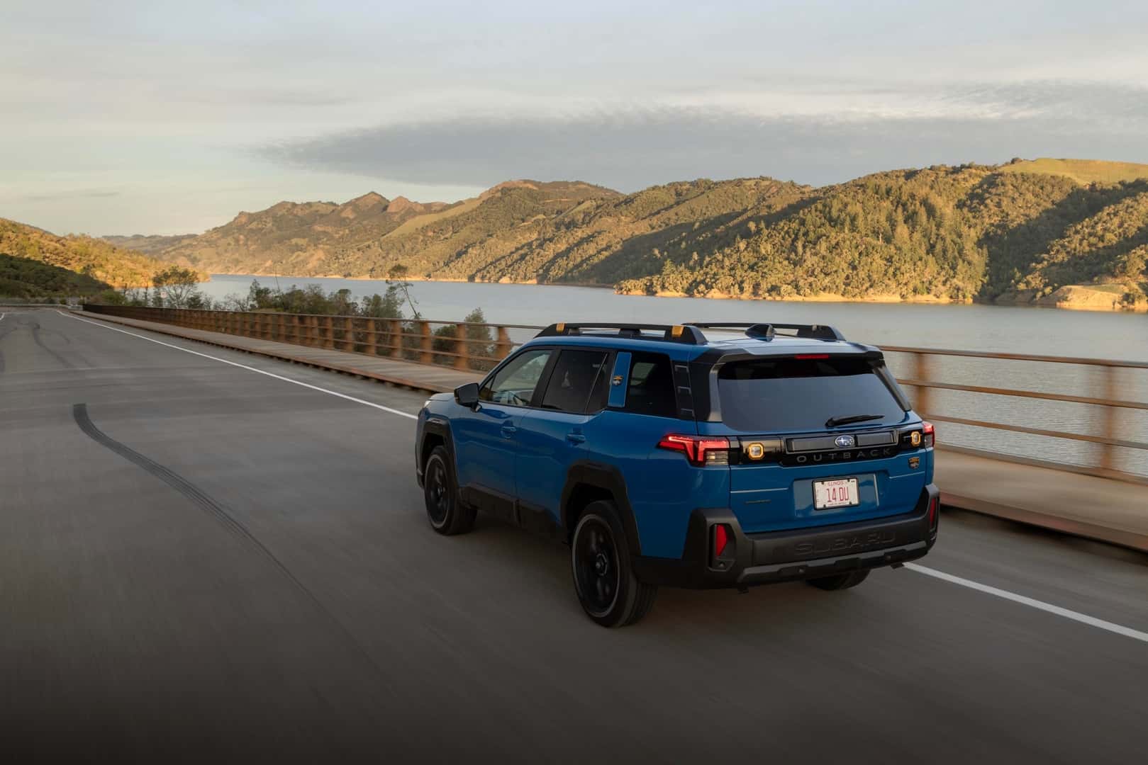 The Adventurous And Outdoor Loving 2026 Subaru Outback Wilderness, Driving Calmly On A Highway Past A Sparkling River And Vast Mountains