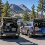 2026 Subaru Forester and 2026 Subaru Outback at a Lake Tahoe family outing parking lot, rear hatches open with gear