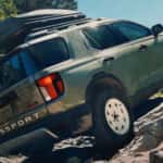 A green Honda Passport with camping accessories on the roof driving up a rocky hillside.