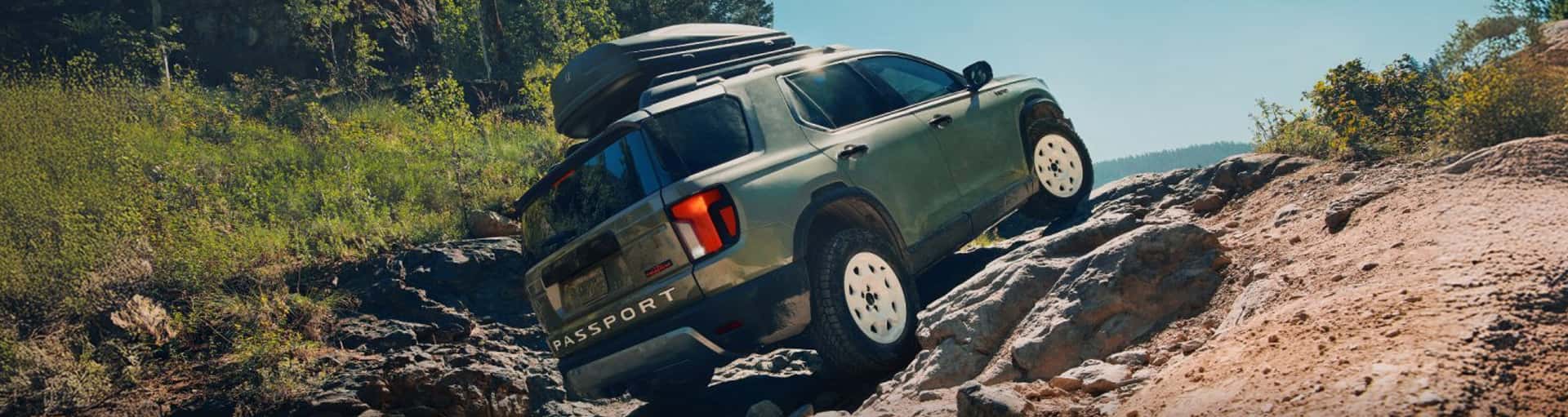 A green Honda Passport with camping accessories on the roof driving up a rocky hillside.