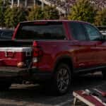 A radiant red Honda Ridgeline midsize pickup truck set up for a lively game-day tailgating scene in a crowded stadium parking lot.
