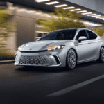 A silver Toyota Camry driving past a lit up city street at night