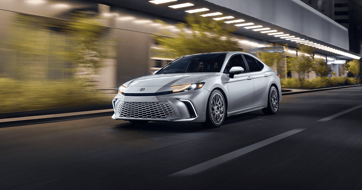 A silver Toyota Camry driving past a lit up city street at night