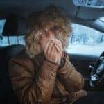 Man in down jacket tries to keep warm and not freeze in his stalled car in winter. The concept of a dangerous accident or heater failure in the cold season