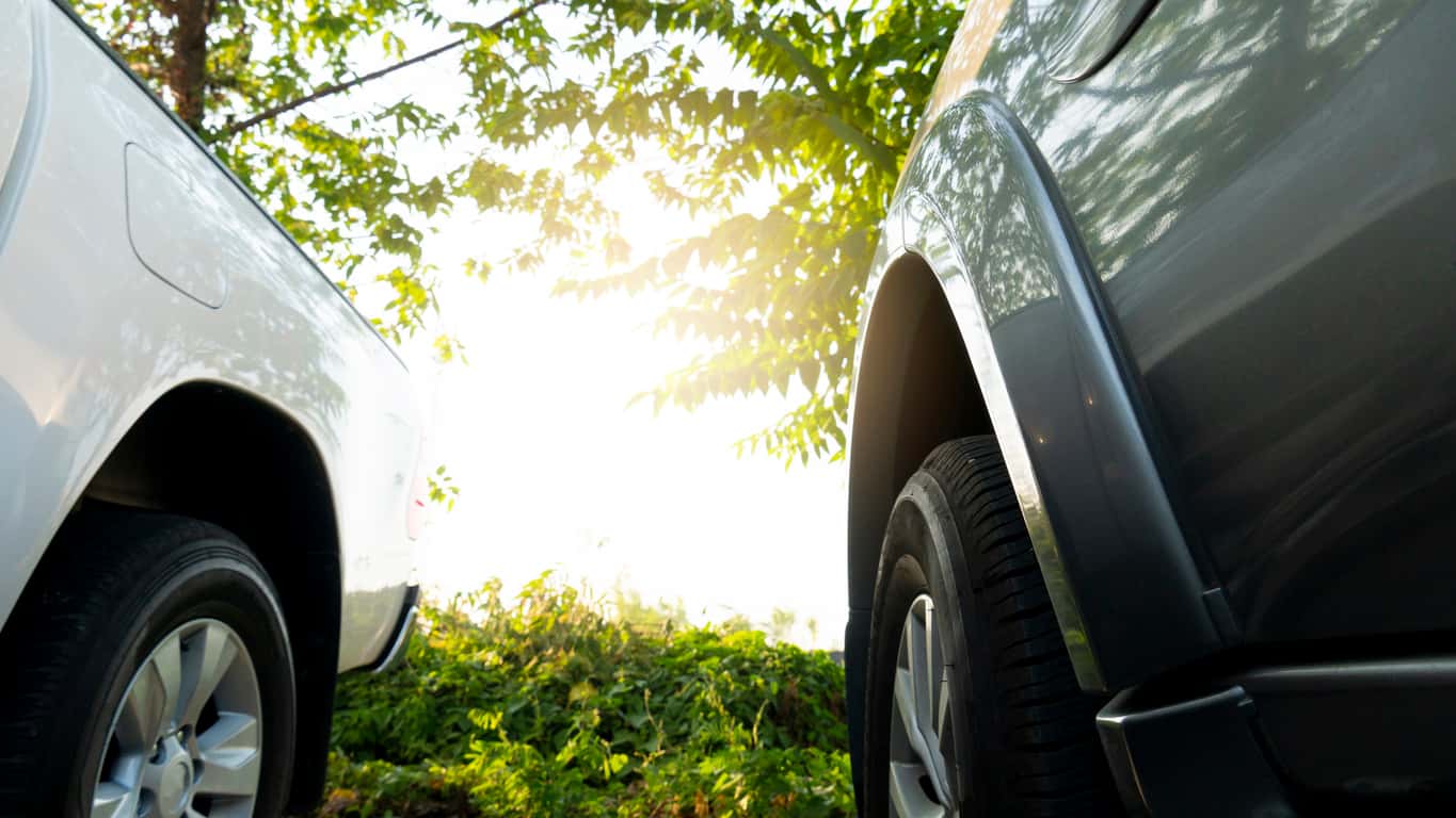 Low angle view of two vehicles' tires facing a sunlit field