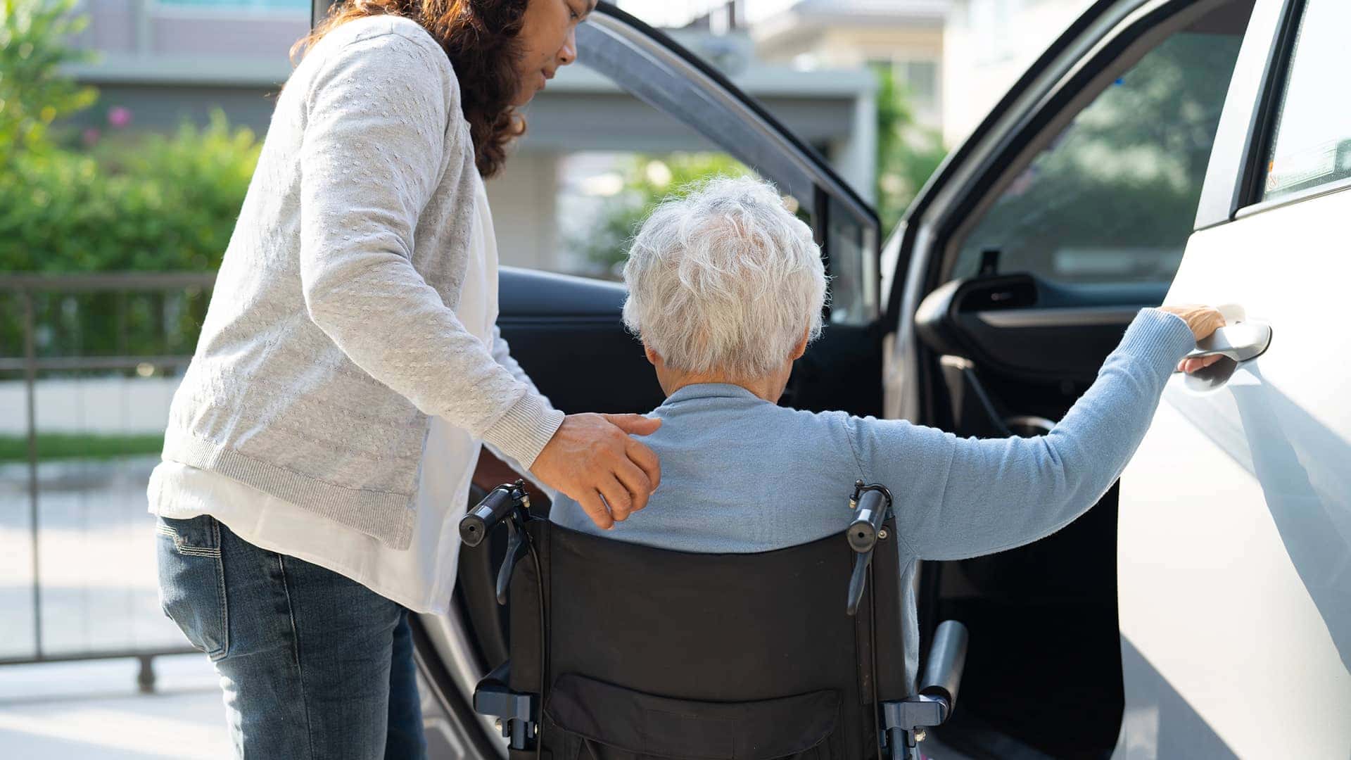 woman helping elderly woman in wheelchair into vehicle