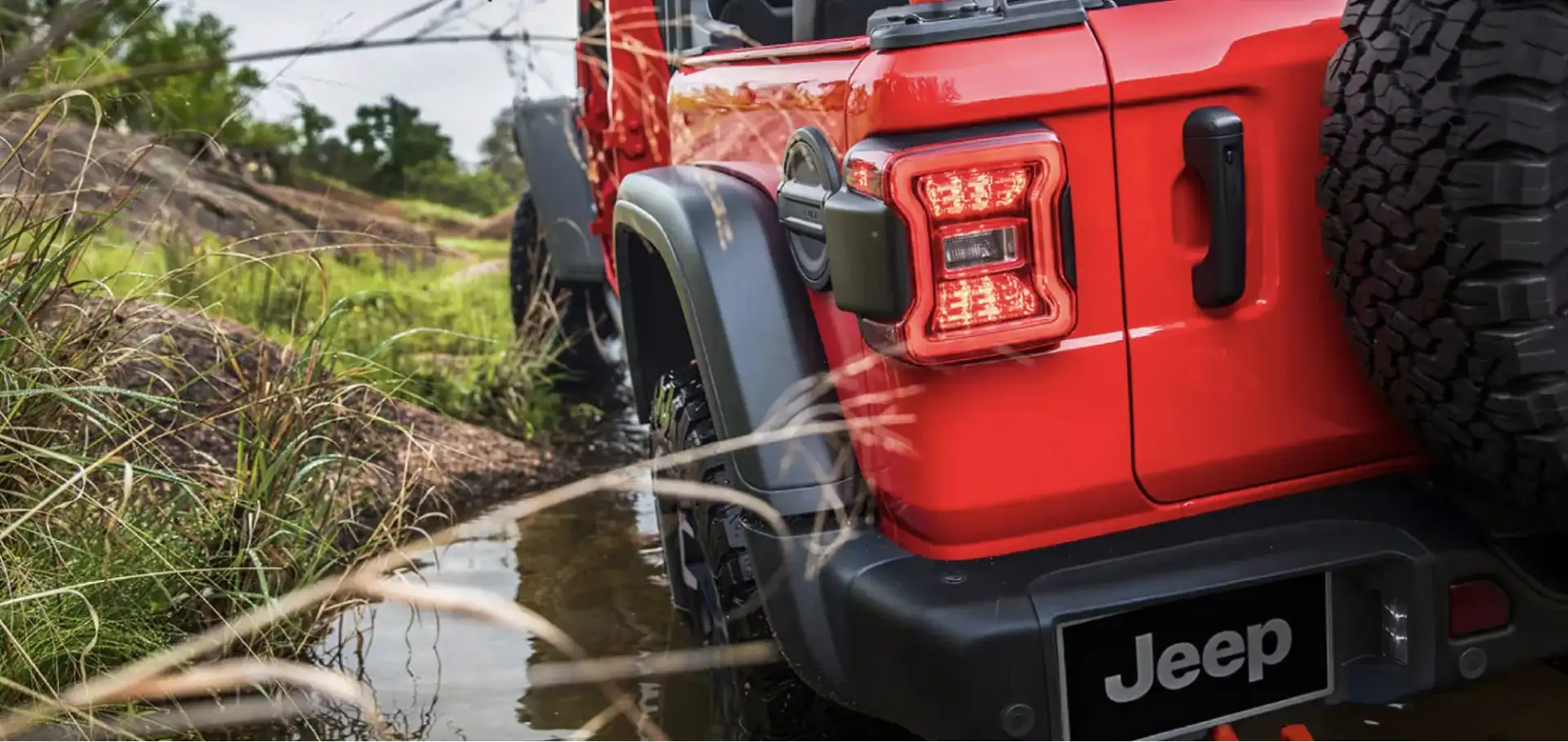 The 2026 Jeep Wrangler crawling through shallow water on a muddy off-road trail