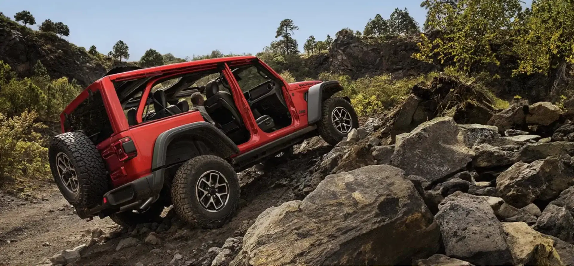 The Jeep Wrangler Rubicon with doors and top removed rock crawling over large boulders on a rugged off-road trail