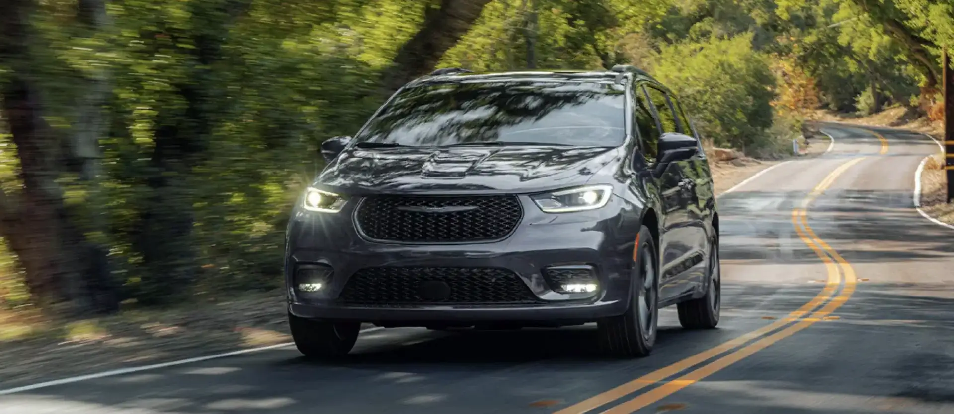 The 2026 Chrysler Pacifica driving along a curving, tree-lined road