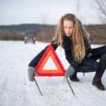 Young woman setting up a warning triangle and calling for assistance after her car broke down in the middle of nowhere on a freezing winter day