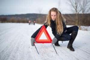Young woman setting up a warning triangle and calling for assistance after her car broke down in the middle of nowhere on a freezing winter day