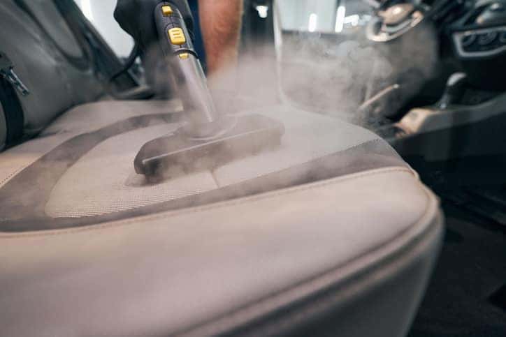 Professional car seat wash with steam cleaner closeup. Detailing of cabin. Deep cleanup from dust