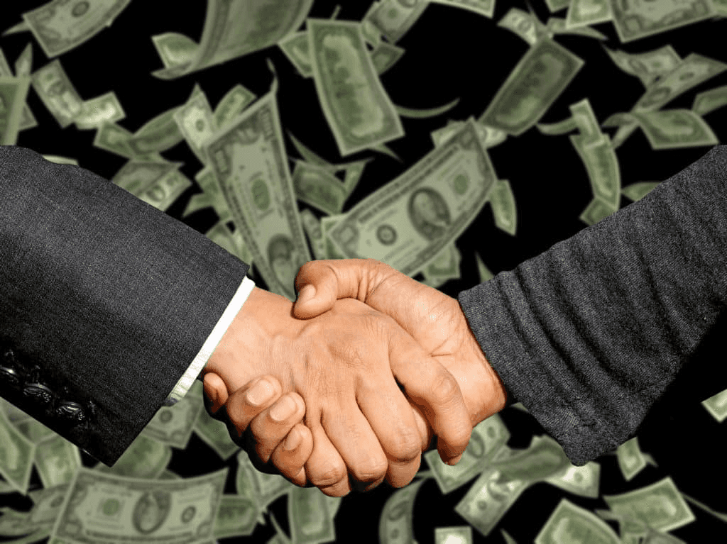 Two people shaking hands while money falls around them