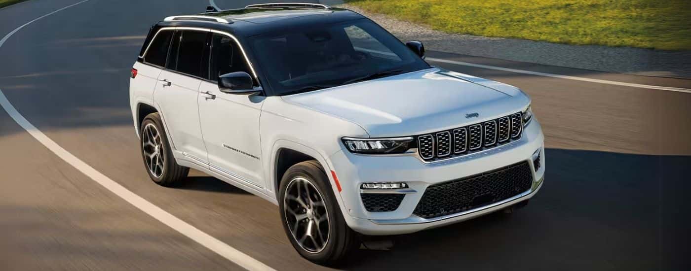 White 2025 Jeep Grand Cherokee driving on a winding road.