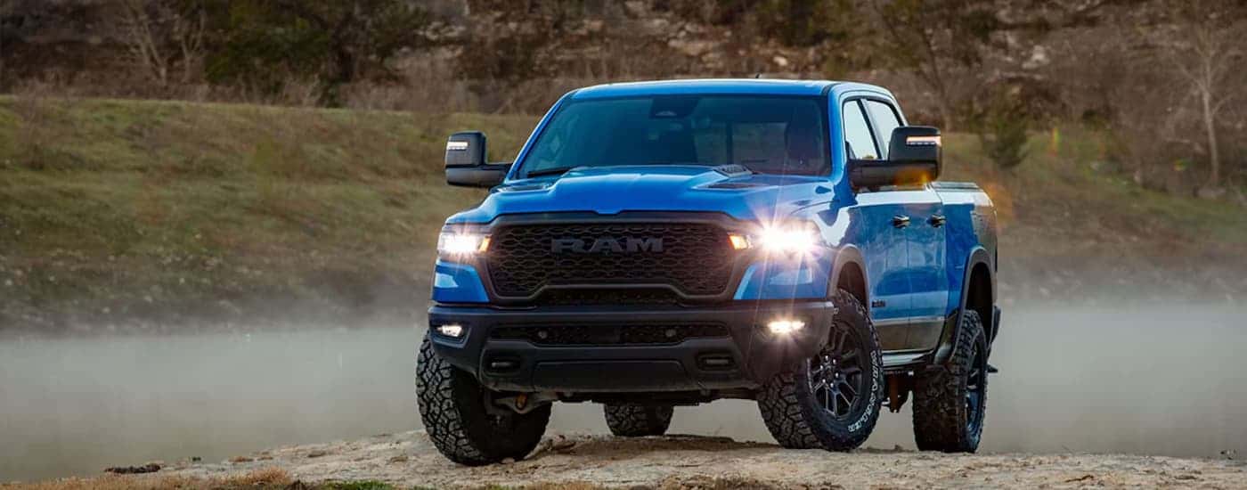 A blue 2025 Ram 1500 Revel parked on gravel at a Ram dealer.