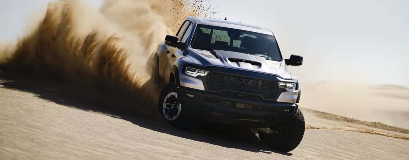A silver 2025 Ram 1500 RHO kicking up dirt off-road.