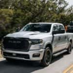 A silver 2025 Ram 1500 towing a trailer on a highway.